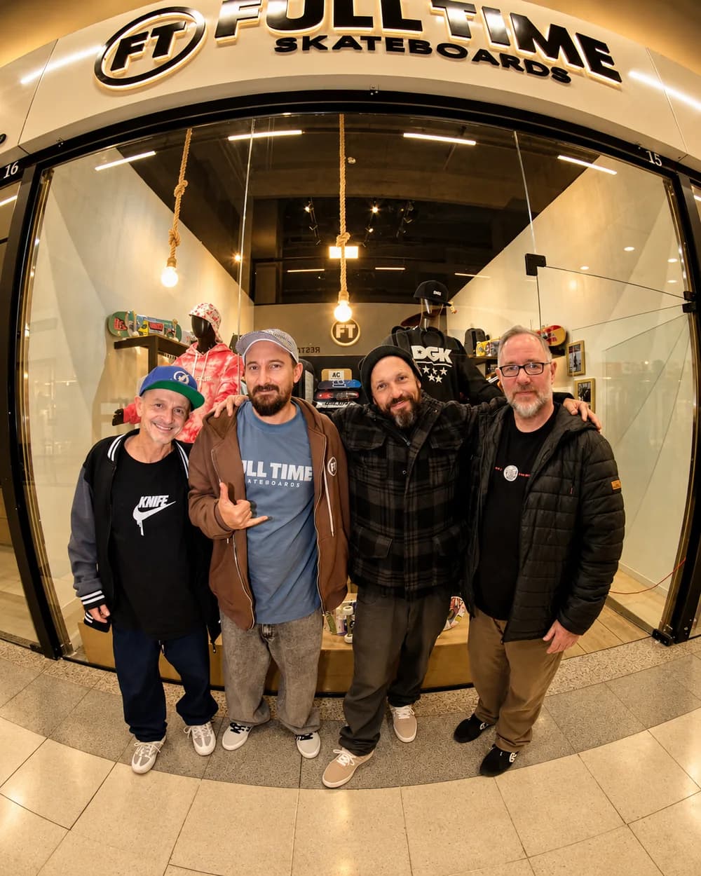 Anderson Camargo e três amigos abraçados na porta da Full Time, com a vitrine acesa atrás